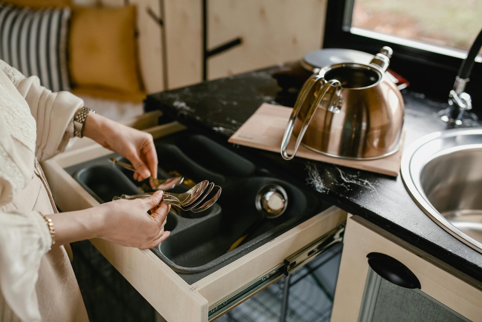 A person efficiently organizes silverware in a minimalist kitchen setting over a drawer dividers